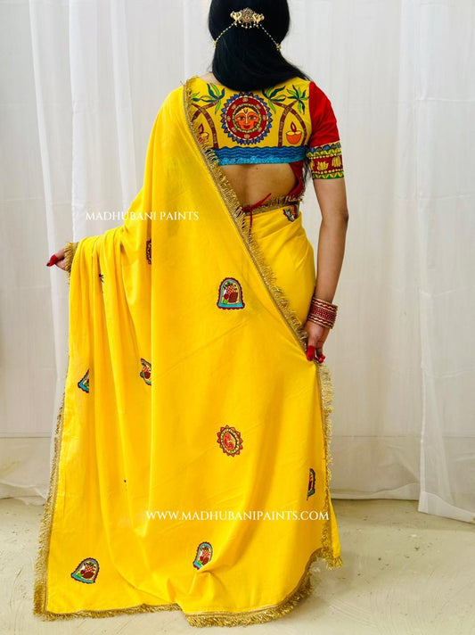 A woman shown from the back wearing a bright yellow chhath puja saree with a heavily madhubani painting red, blue, and gold blouse.