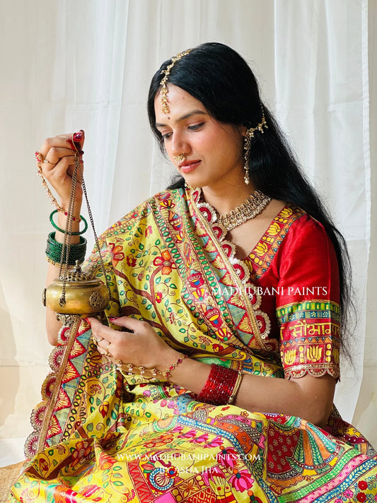 Yellow Devi Ki Sawari Madhubani saree with traditional doli procession painting and decorative lotus border beside festive puja flowers.