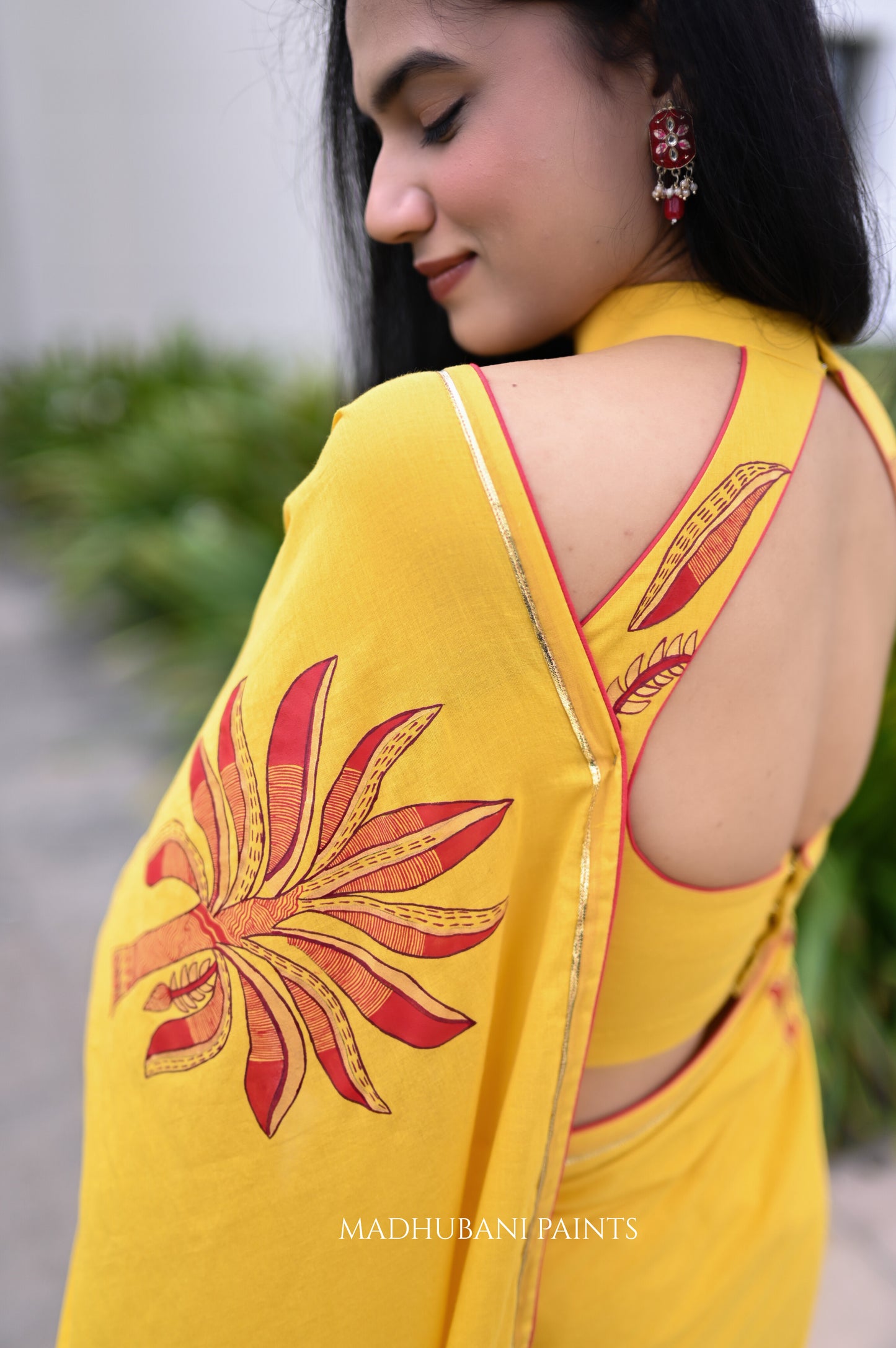 Woman wearing a yellow saree with red floral patterns, standing outdoors.