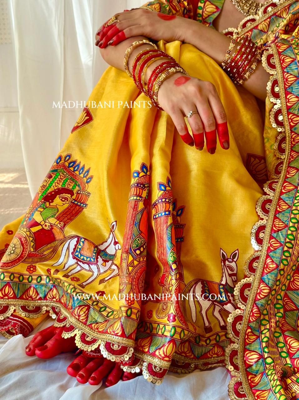 A close-up of a person wearing a bright yellow traditional saree with colorful hand-painted motifs 