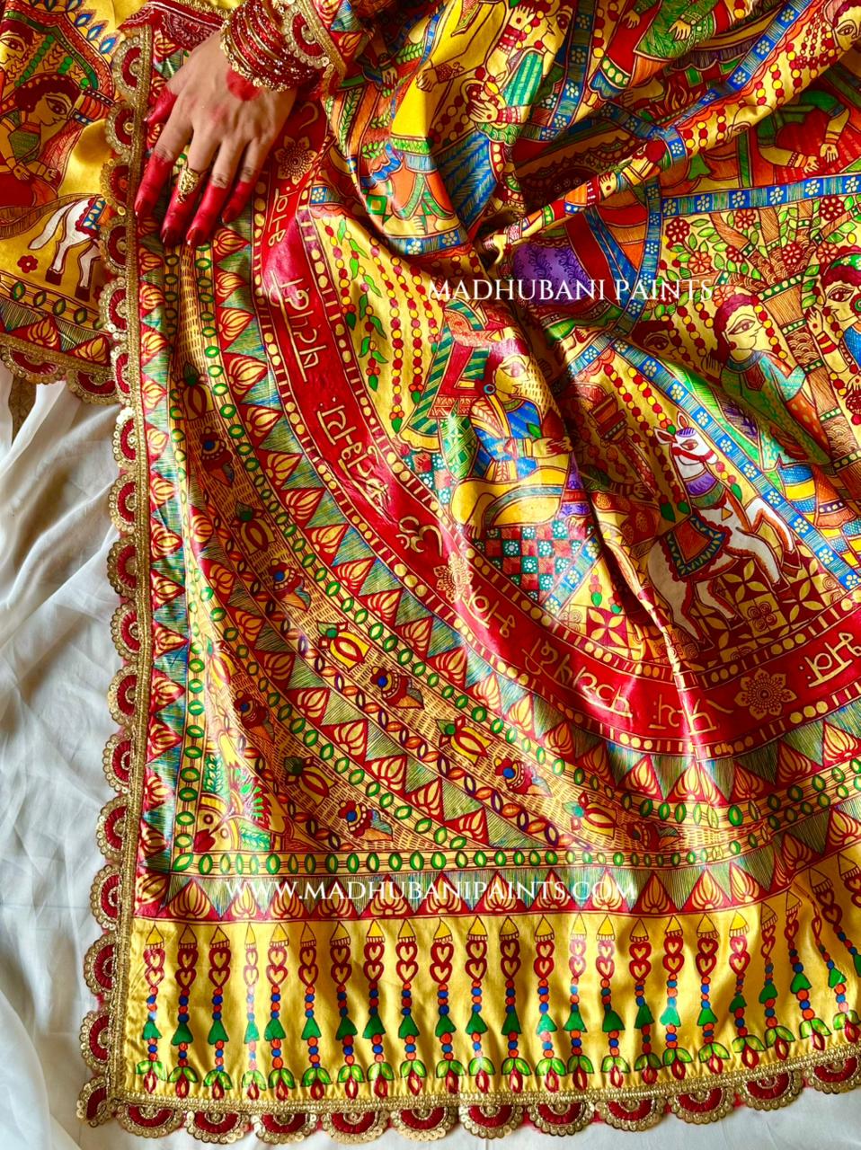 A close-up of a richly painted sari, featuring a vibrant multicolor hand-painted madhubani painting design with red, yellow, green, and blue motifs.