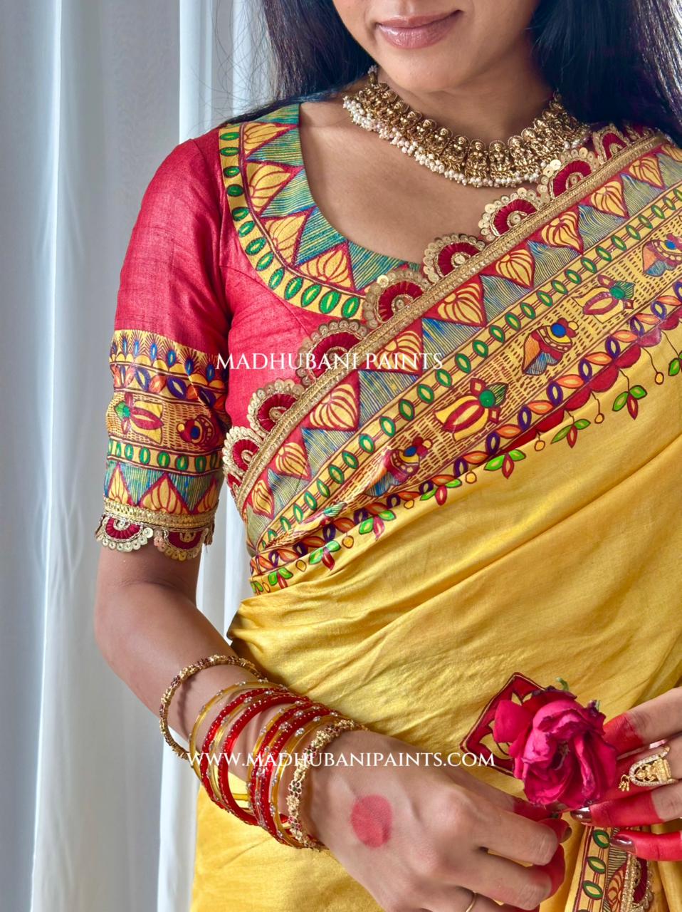 A close-up of a woman wearing a traditional madhubani painting saree with a bright yellow body, a red blouse, and intricate multicolor artwork for wedding 