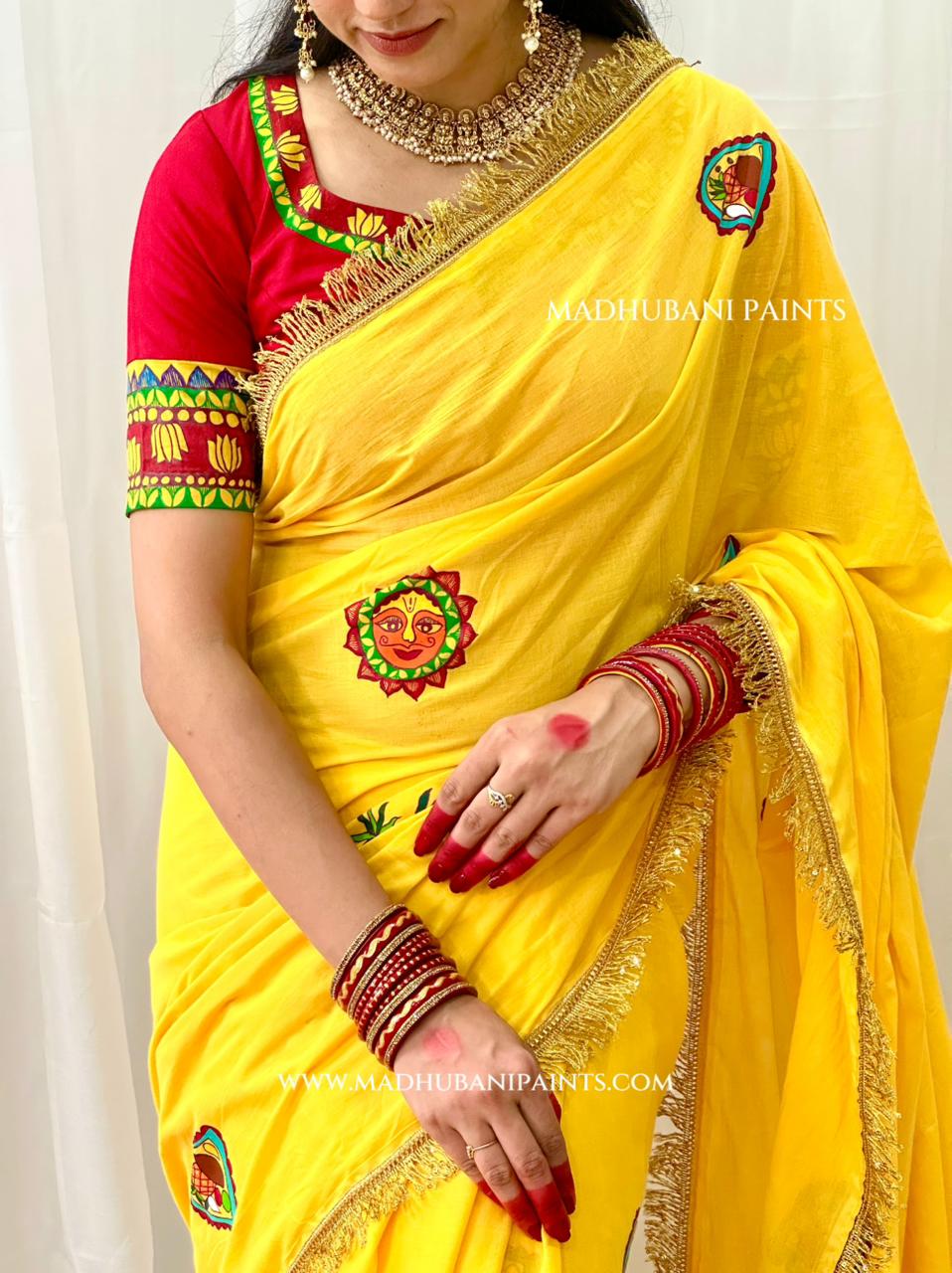 A woman wearing a bright yellow saree with a red blouse, decorated with gold zari embroidery and colorful floral motifs. The image features a watermark for Madhubani Paints.