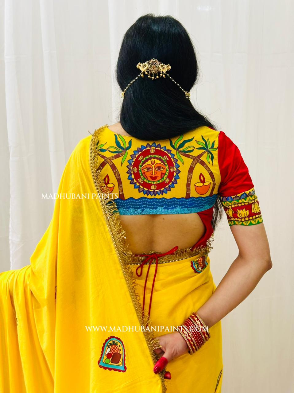 A woman shown from the back wearing a bright yellow chhath puja saree with a highly detailed, colorful madhubani painting blouse in contrast red color. The blouse features a central deity motif, palm trees, a blue wave border, and red sleeves with gold and green patterns.
