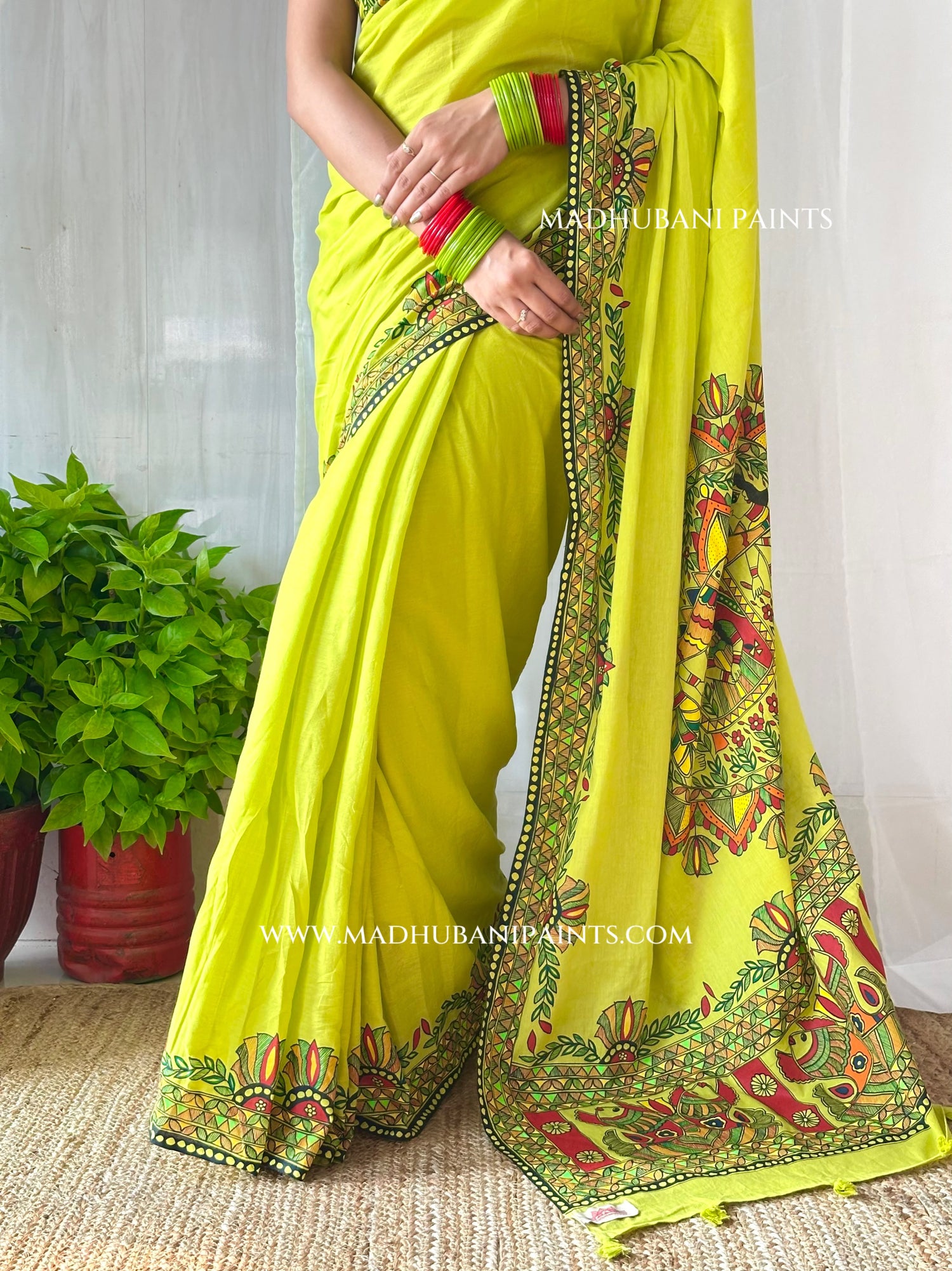 A woman wearing a bright yellow-green saree with ornate multicolor floral border prints and green bangles