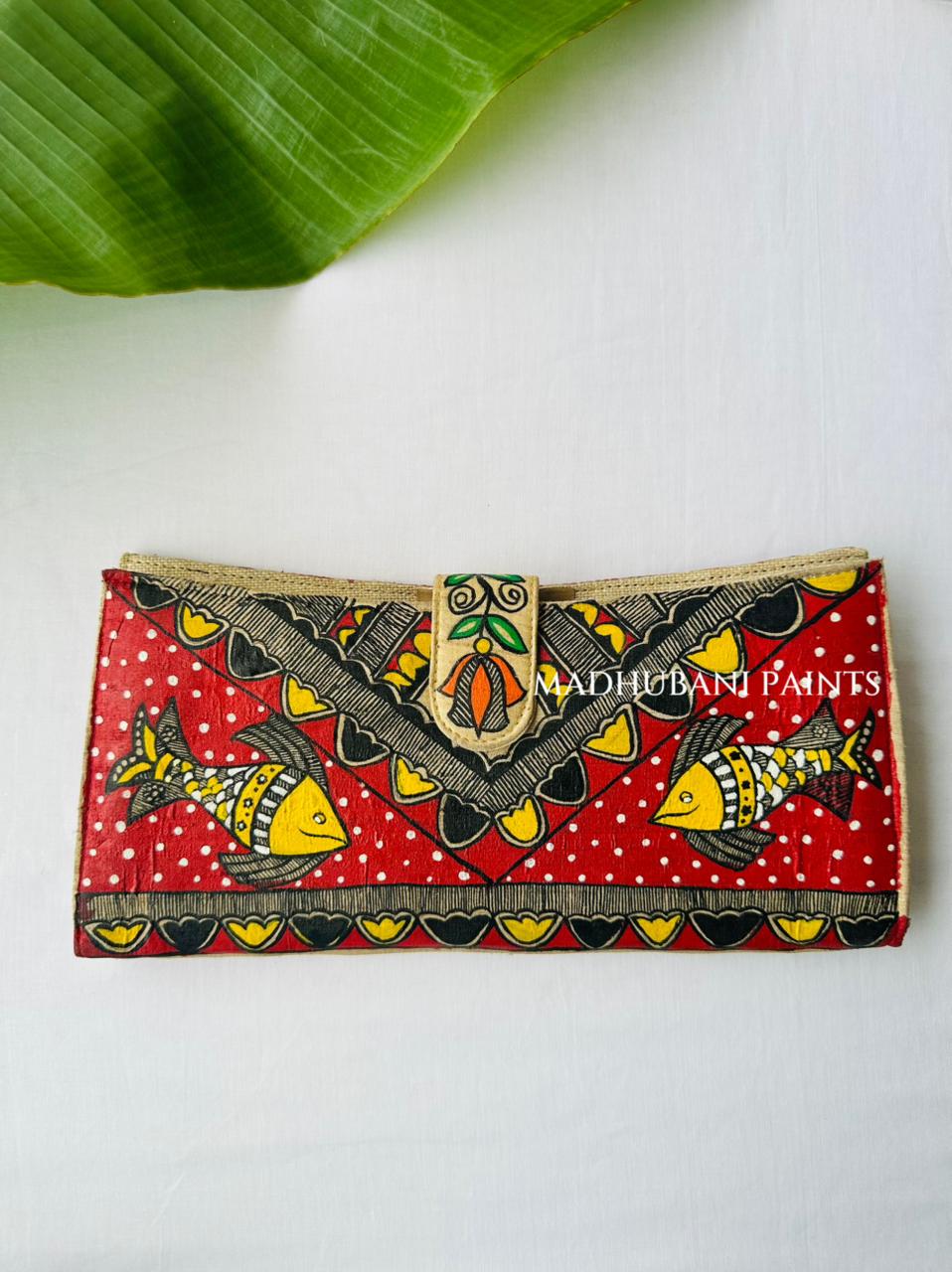 Hand-painted Madhubani clutch in orange with a bold lotus pattern and two fish, a matching lotus motif on the tab closure