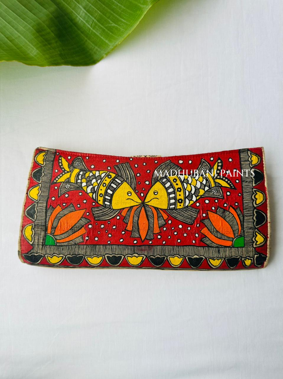 Hand-painted Madhubani clutch in orange with a bold lotus pattern and two fish, a matching fish motif on the tab closure