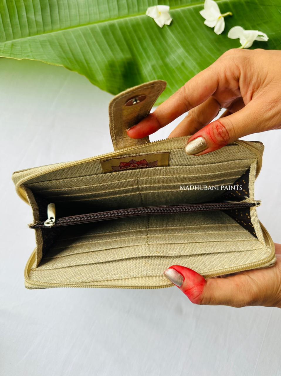 A beige canvas zippered wallet held open by two hands, showing its interior card slots and zipper compartments. 