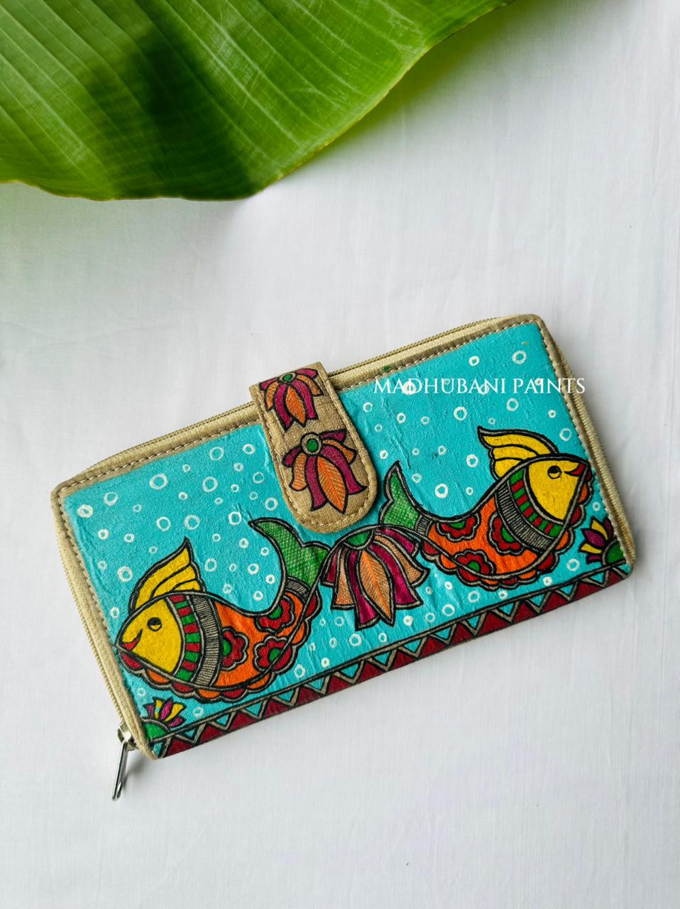 Front View of the Hand-painted Madhubani clutch in turquoise with two orange-and-yellow fish swimming apart, a lotus flower on the tab closure, and a red triangle border along the base