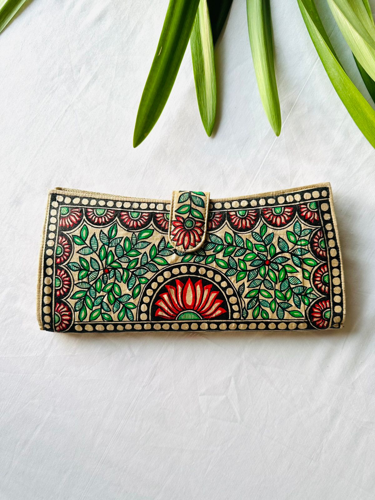 Hand-painted Madhubani clutch in cream with a red lotus in a round medallion at the center, flanked by green leaf sprays and small lotus flowers in each corner.
