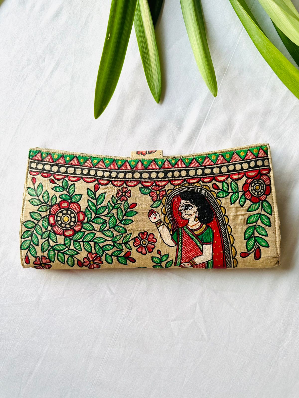 Hand-painted Madhubani clutch in cream with a traditionally dressed woman in profile, surrounded by red flowers and green leaves