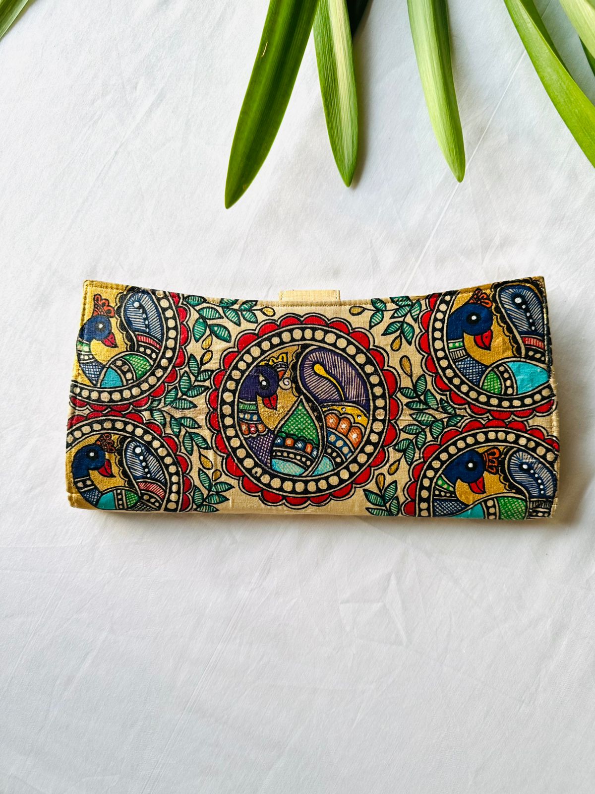 Hand-painted Madhubani clutch in gold with three peacocks set in round medallions among green leaves