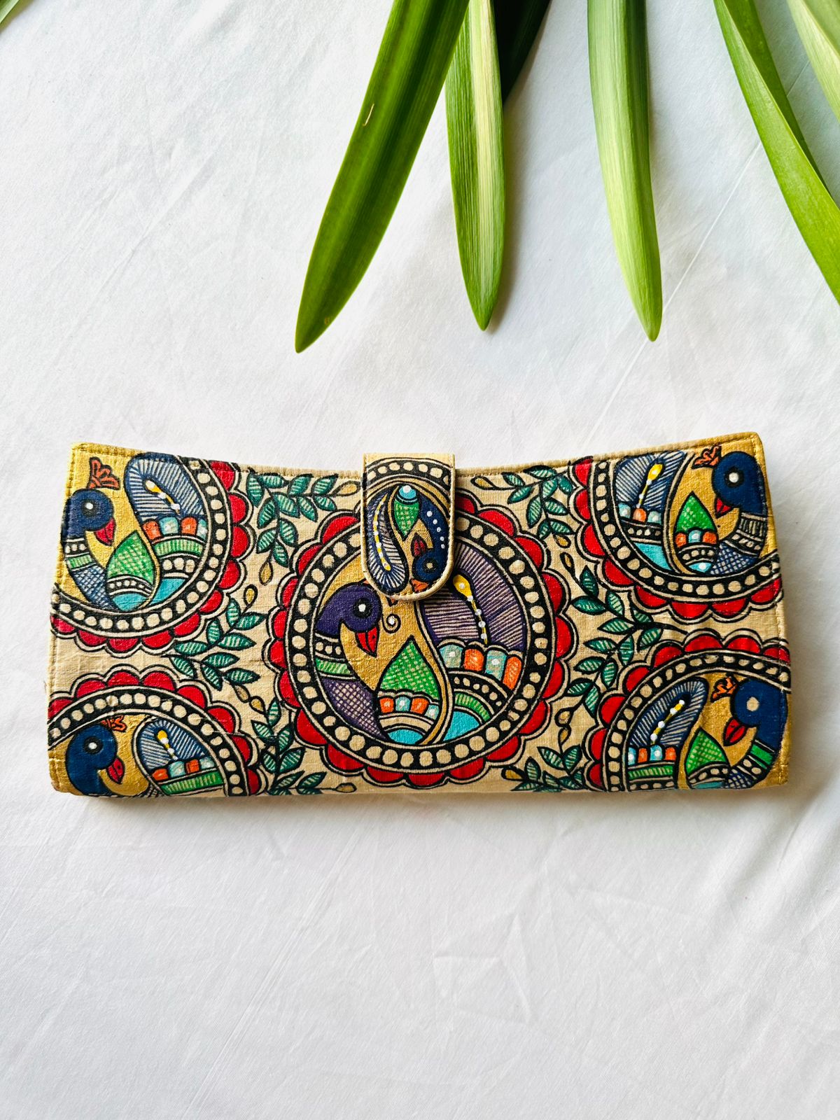 Hand-painted Madhubani clutch in gold with three peacocks set in round medallions among green leaves