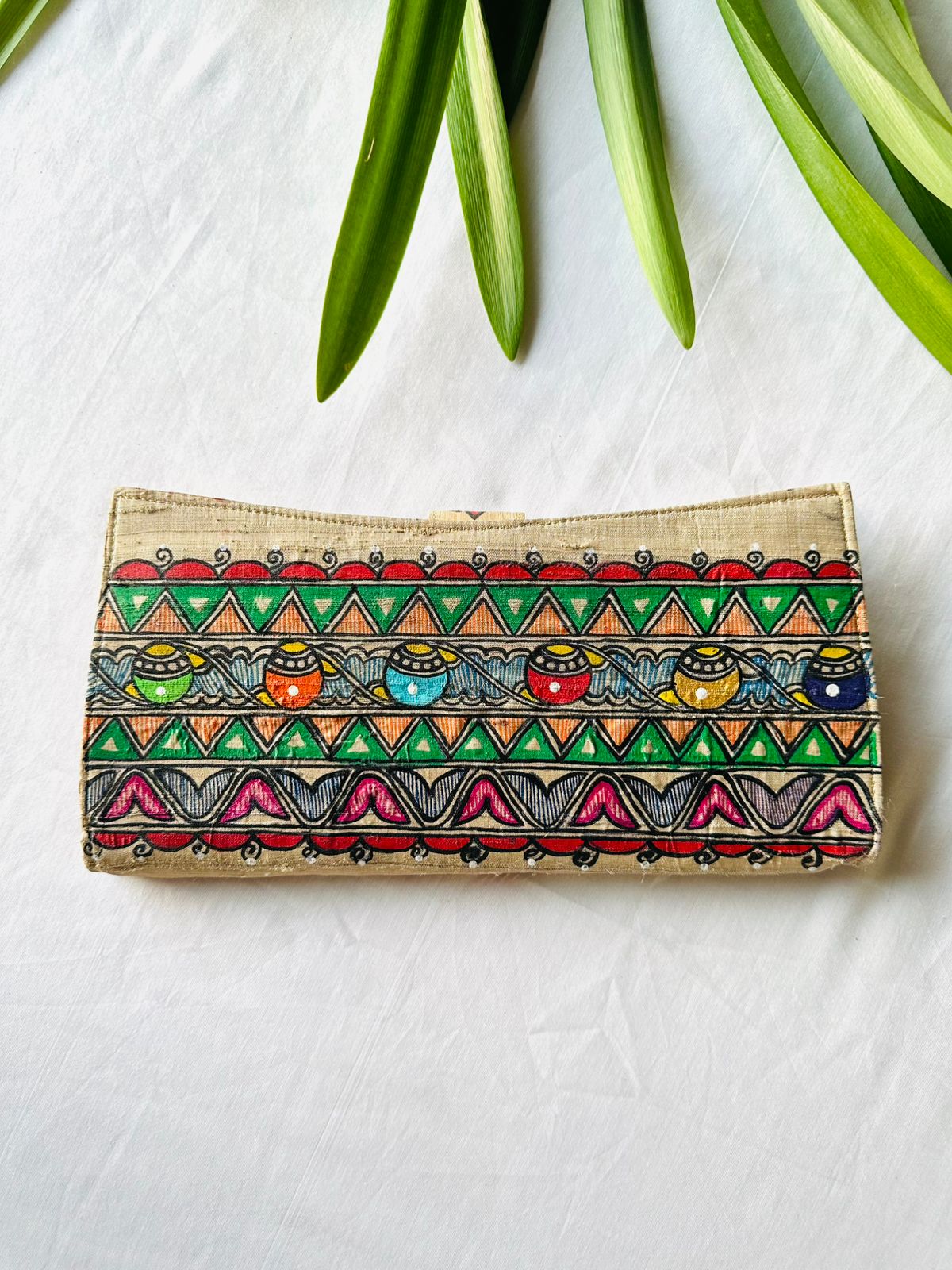back side of Hand-painted Madhubani clutch in beige with a row of small colorful pots on a wave pattern, framed by green triangle borders.