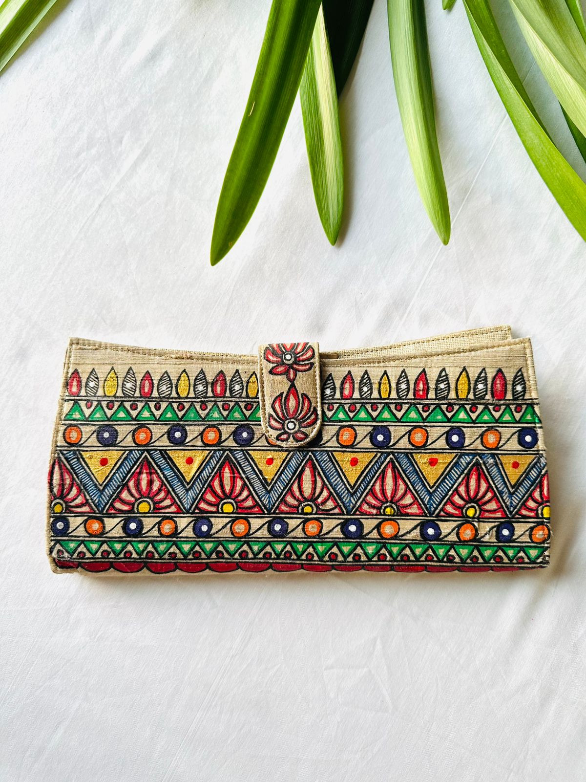 Hand-painted Madhubani clutch in beige with a row of small colorful pots on a wave pattern, framed by green triangle borders.