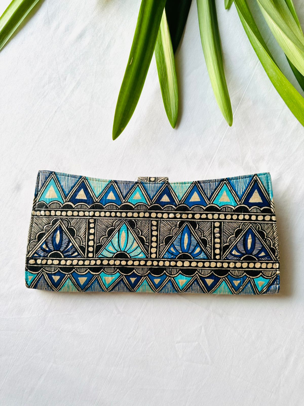 Hand-painted Madhubani clutch in shades of blue and black with a zigzag chevron pattern and lotus flowers set inside the triangles