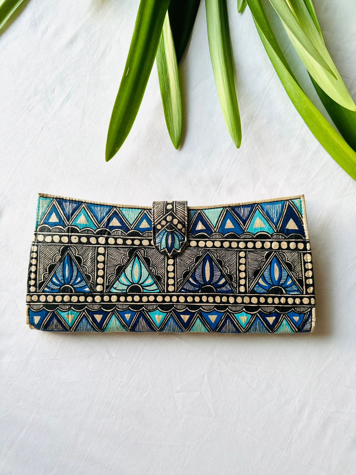 Hand-painted Madhubani clutch in shades of blue and black with a zigzag chevron pattern and lotus flowers set inside the triangles