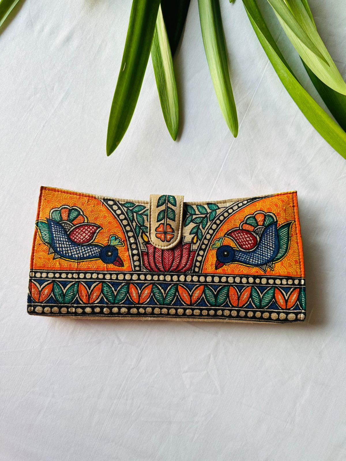 Hand-painted Madhubani clutch in vivid orange with two birds facing a central lotus flower beneath a leafy arch