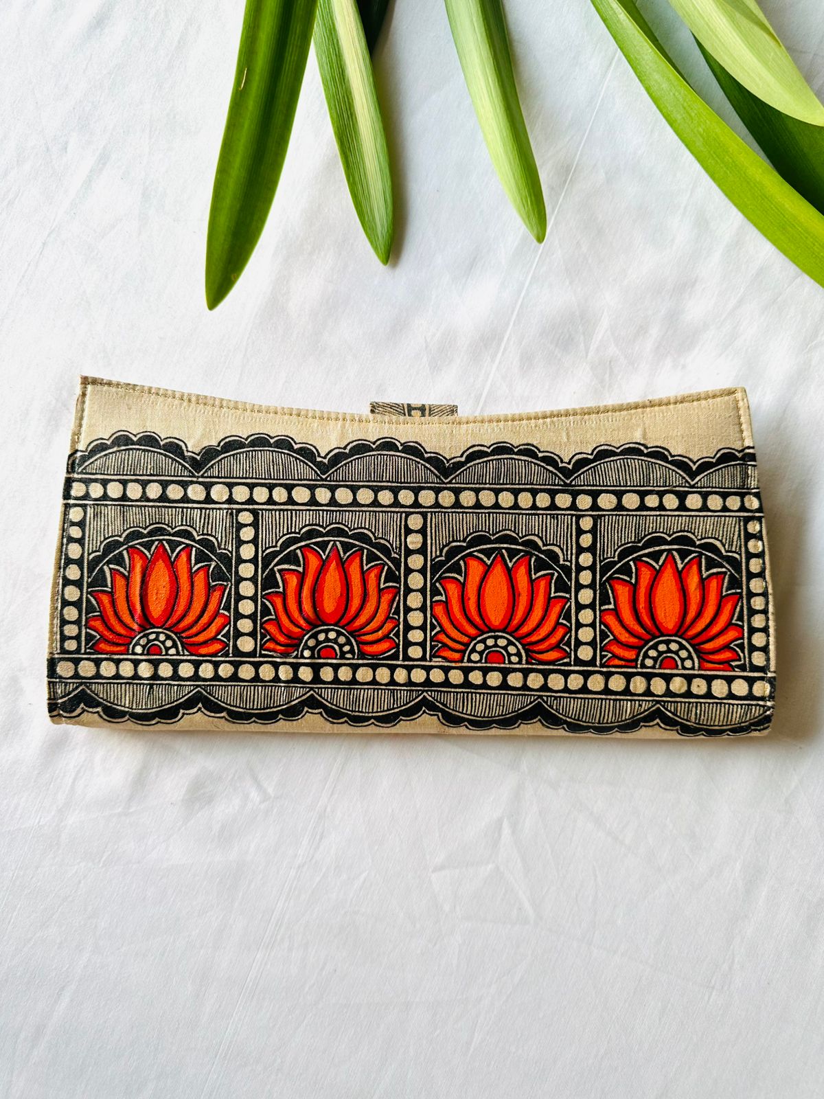 Hand-painted Madhubani clutch in black and cream with a row of four orange-red lotus flowers set in scalloped arches