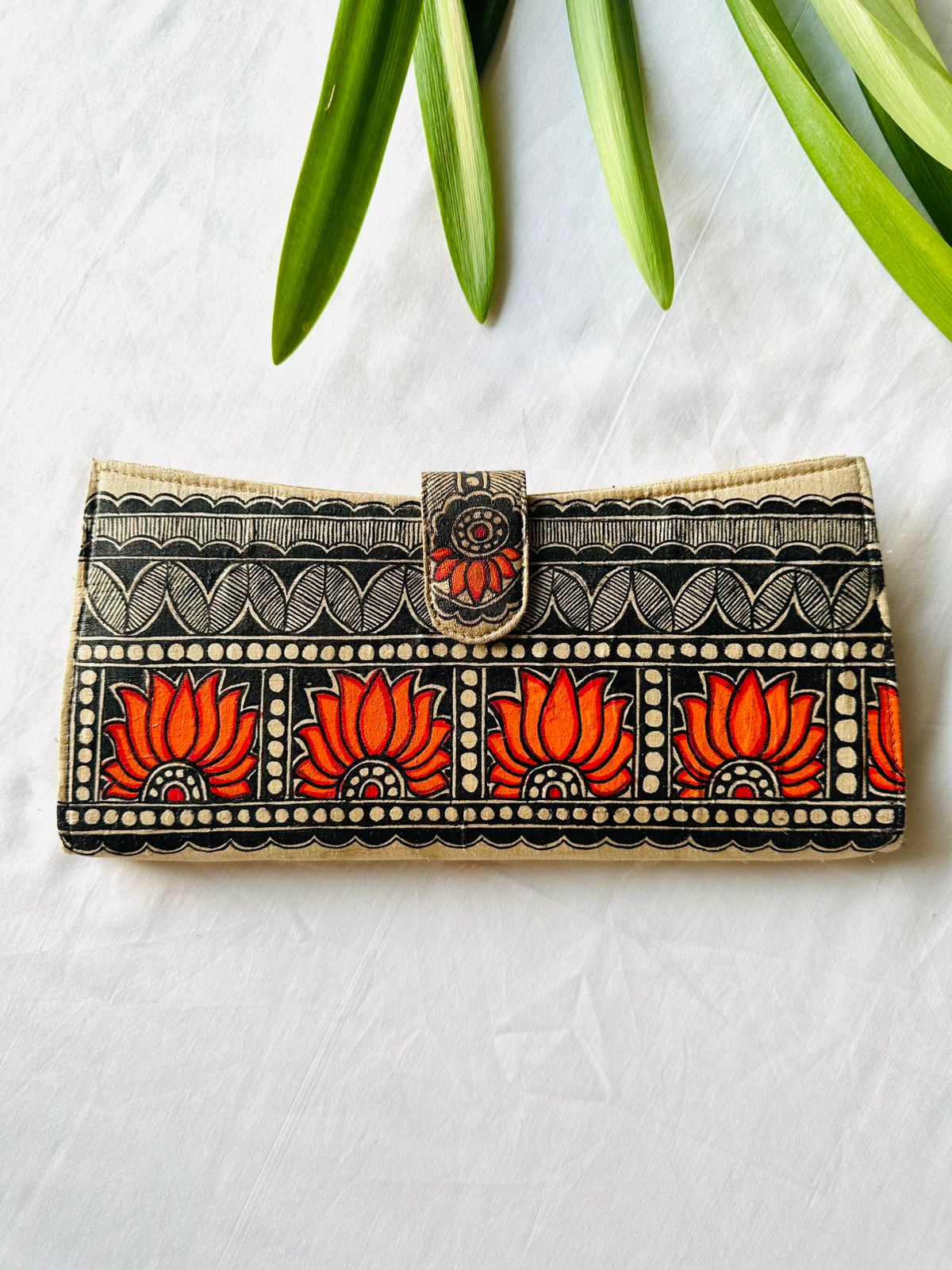 Hand-painted Madhubani clutch in black and cream with a row of four orange-red lotus flowers set in scalloped arches