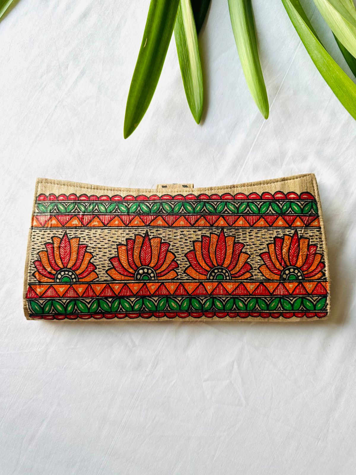 Hand-painted Madhubani clutch in beige with four orange-red lotus flowers, framed by a green leaf border and orange triangle stripes