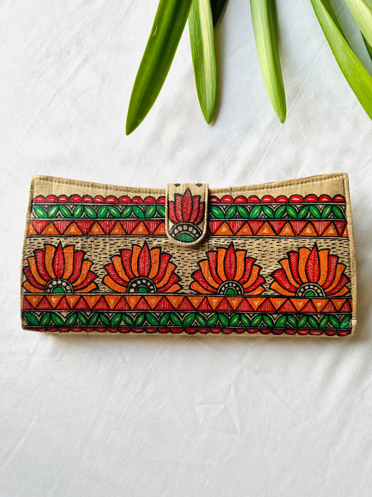 Hand-painted Madhubani clutch in beige with four orange-red lotus flowers, framed by a green leaf border and orange triangle stripes