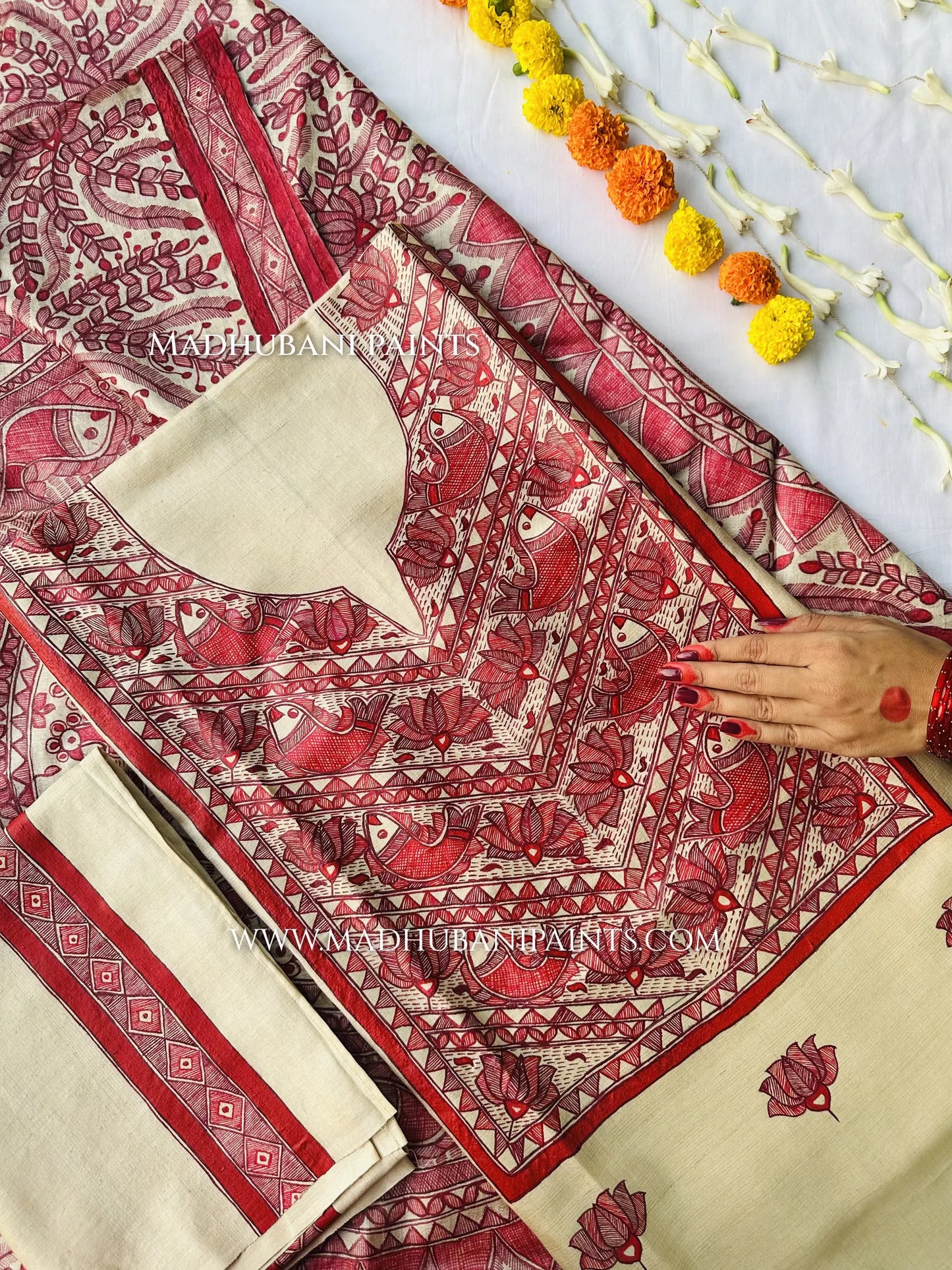 Cream dupatta hand-painted with a large red circular Madhubani mandala, fish motifs and a leafy border, beside a string of marigolds.