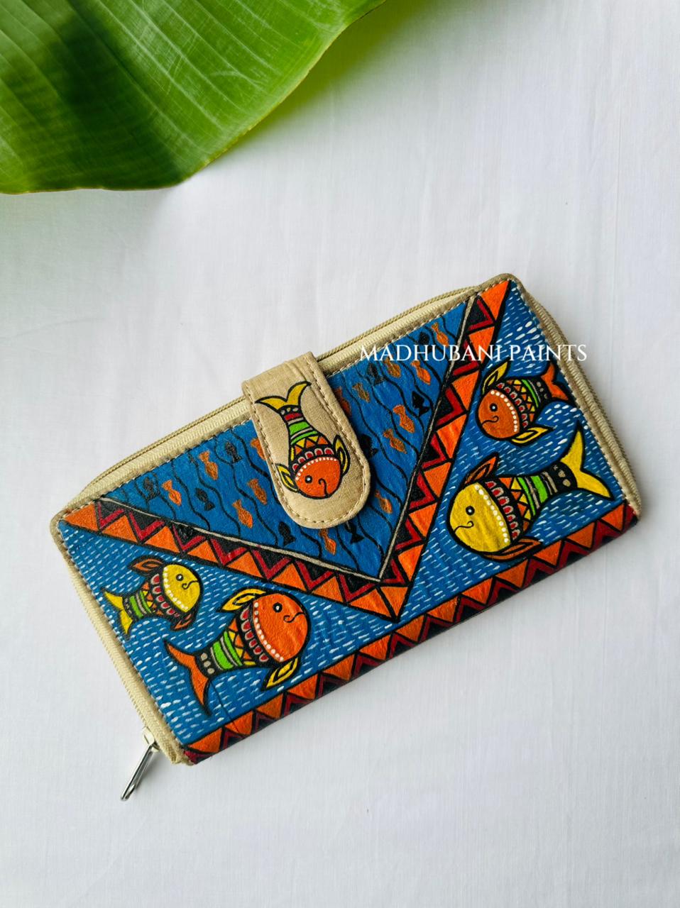 Hand-painted Madhubani clutch with orange and yellow fish swimming on a deep blue dotted background, framed by a chevron border