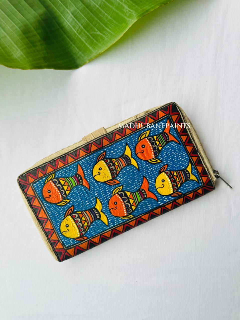 Hand-painted Madhubani clutch with fish set against a diagonal blue and orange geometric pattern, a fish painted on the tab closure
