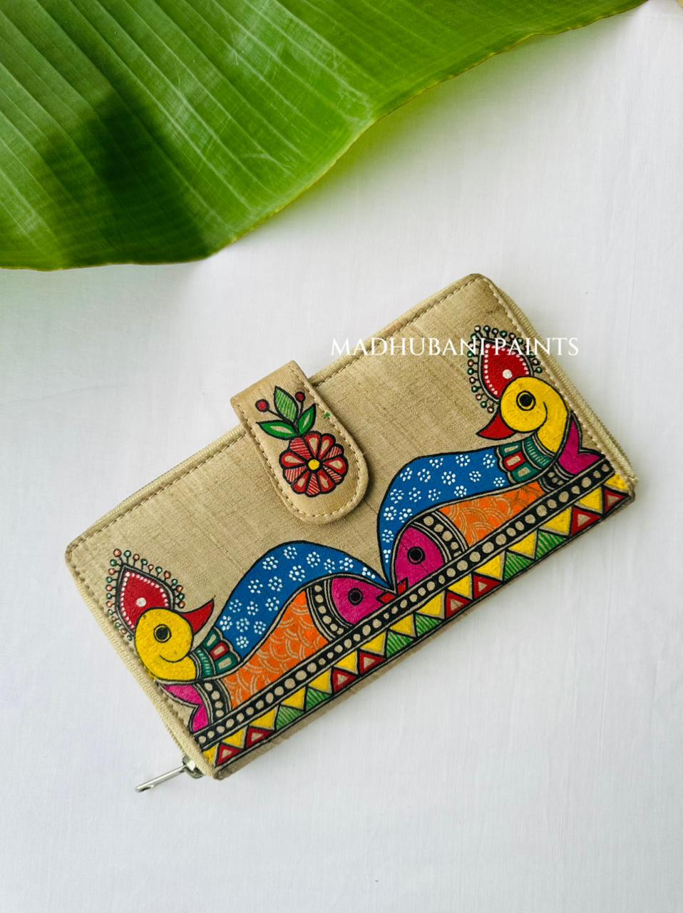 Hand-painted Madhubani clutch with a colorful fish and peacock abordered by triangles, set on a blue dotted background with small lotus flowers
