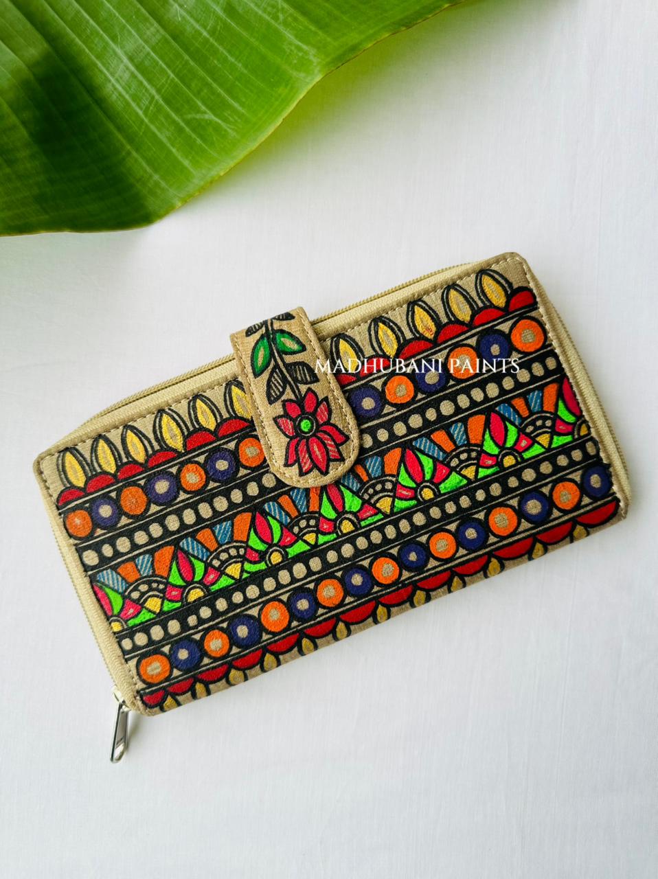 Hand-painted Madhubani clutch with horizontal bands of scalloped petal and fan shapes in red, orange, blue, and green, a pink flower painted on the tab closure