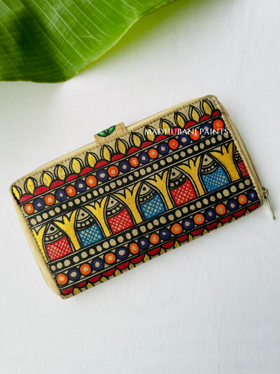 Hand-painted Madhubani clutch with horizontal bands of fish petal and fan shapes in red, orange, blue, and green, a pink flower painted on the tab closure