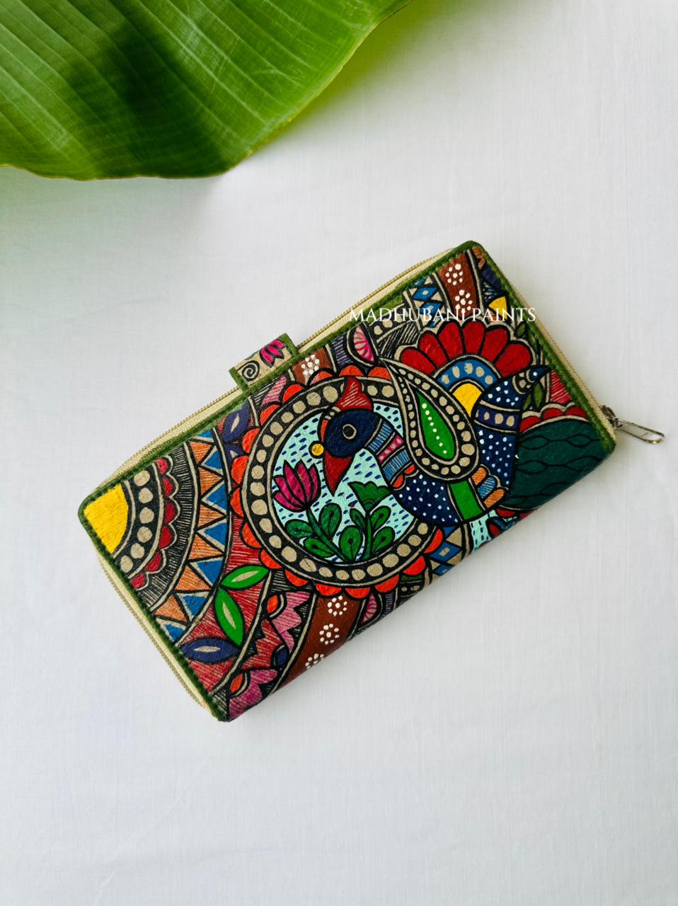 Hand-painted Madhubani clutch with a large colorful peacock in a paisley medallion, a small lotus at its center, beside a radiating sunburst pattern, framed by an olive-green edge