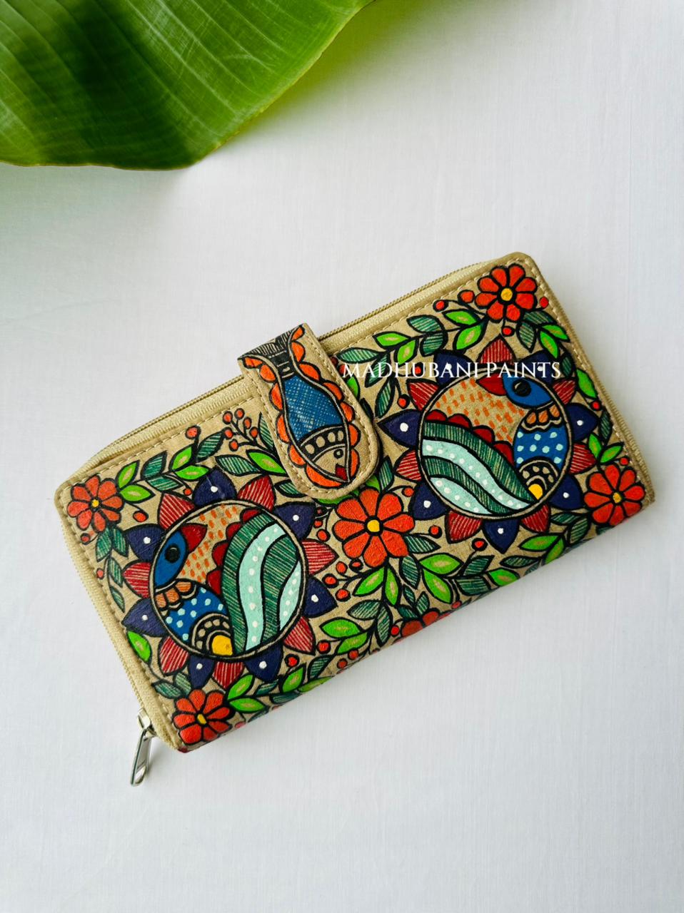 Hand-painted Madhubani clutch in beige with two circular medallions of stylized peacocks in teal, red, and blue, surrounded by orange flowers and green leaves, a small fish painted on the tab closure