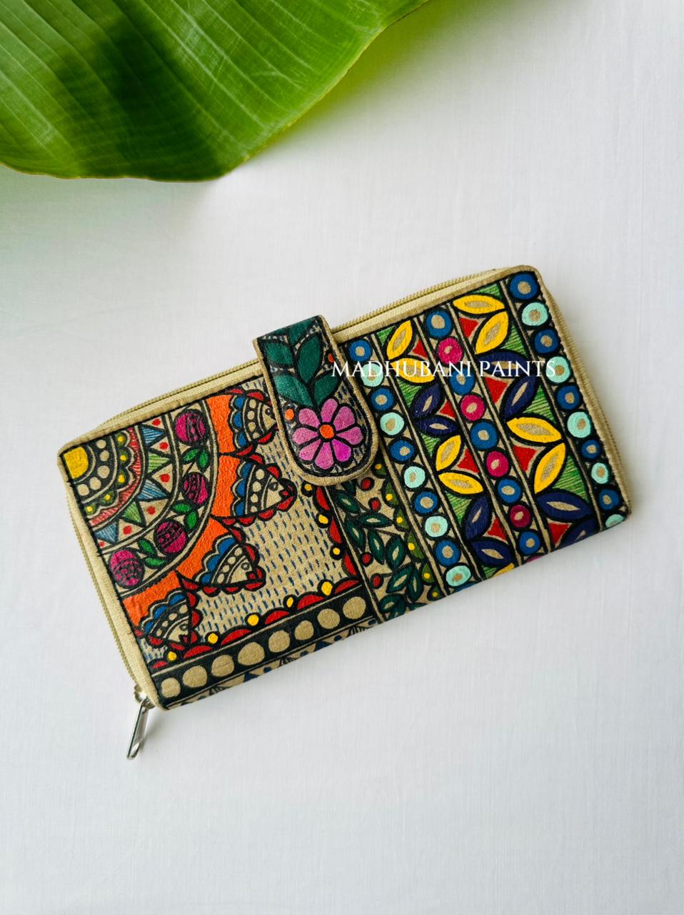 Hand-painted Madhubani clutch with an orange floral mandala on one half and colorful vertical stripes of petals and circles in blue, yellow, and mint on the other, a teal flower on the tab closure
