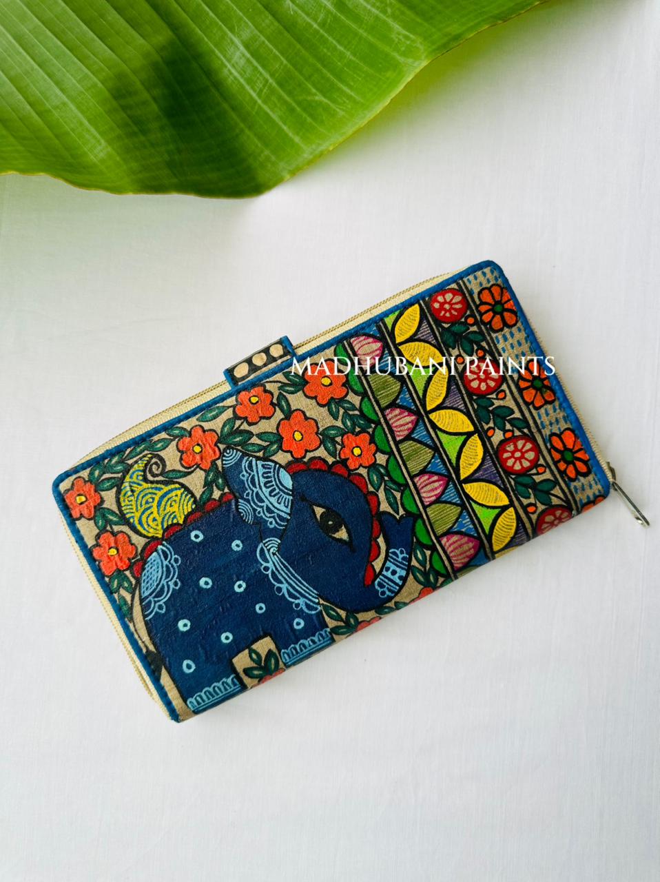 Hand-painted Madhubani clutch with a navy-blue elephant head design, surrounded by a floral border and colorful striped panels, a small lotus painted on the tab closure