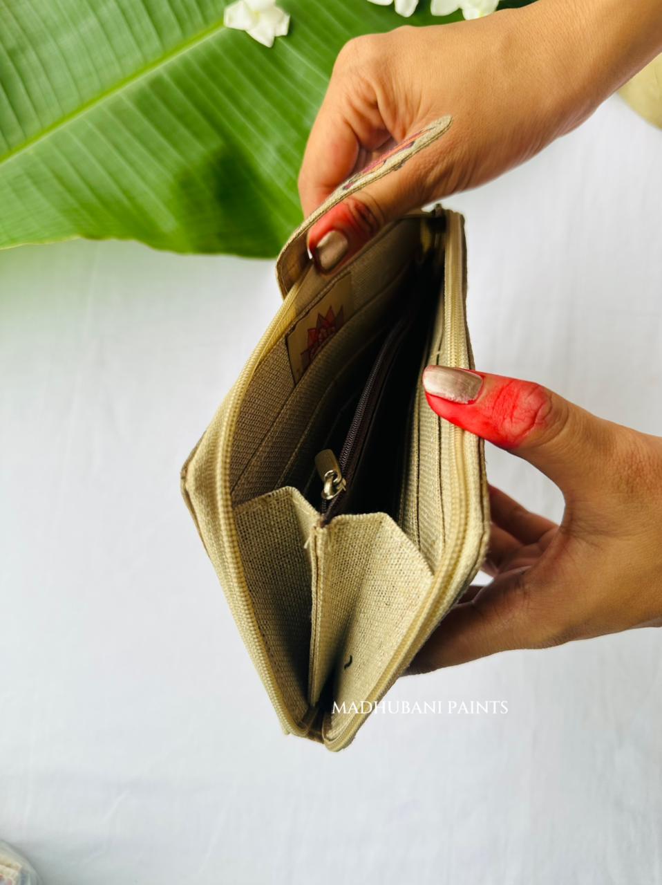 A close-up of a person holding open a beige canvas zippered wallet or card holder, showing its interior compartments.