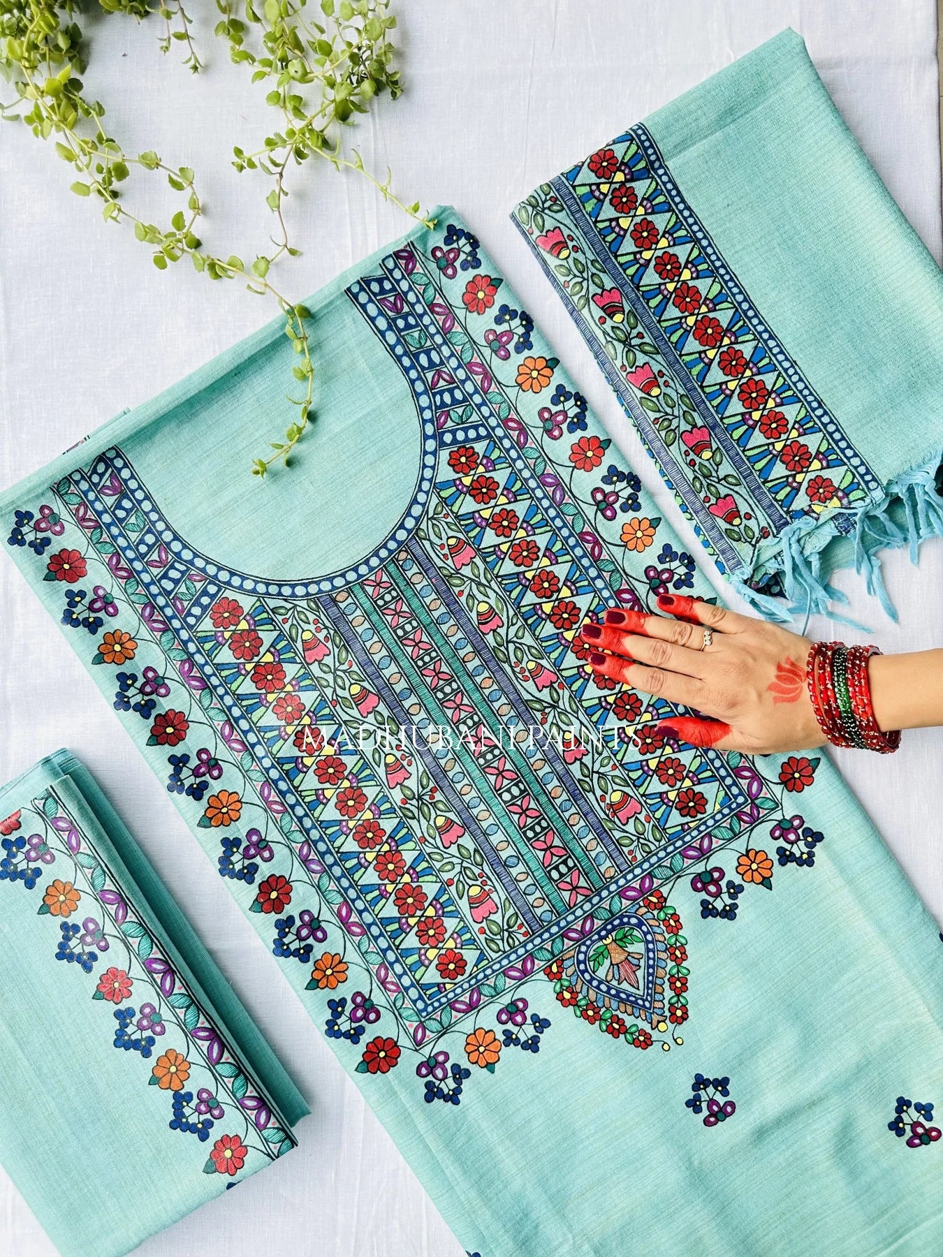 A mint green unstitched salwar kameez suit set with intricate multicolor handpainted madhubani artwork