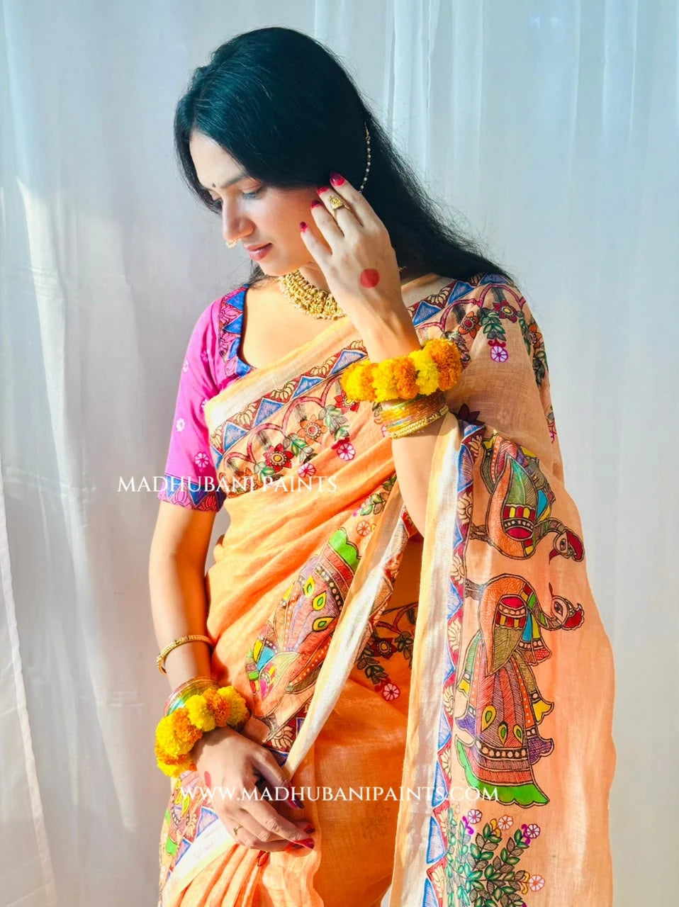 Model wearing a peach hand-painted Madhubani linen saree with traditional peacock artwork and colourful floral designs.
