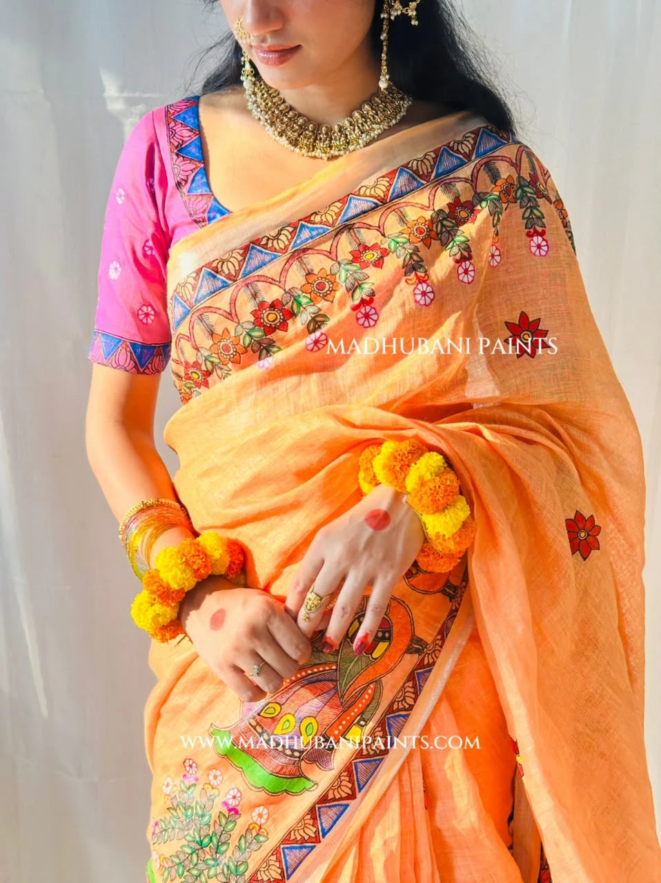 Close-up of pink Madhubani blouse back design paired with peach linen saree featuring traditional peacock and floral painting.