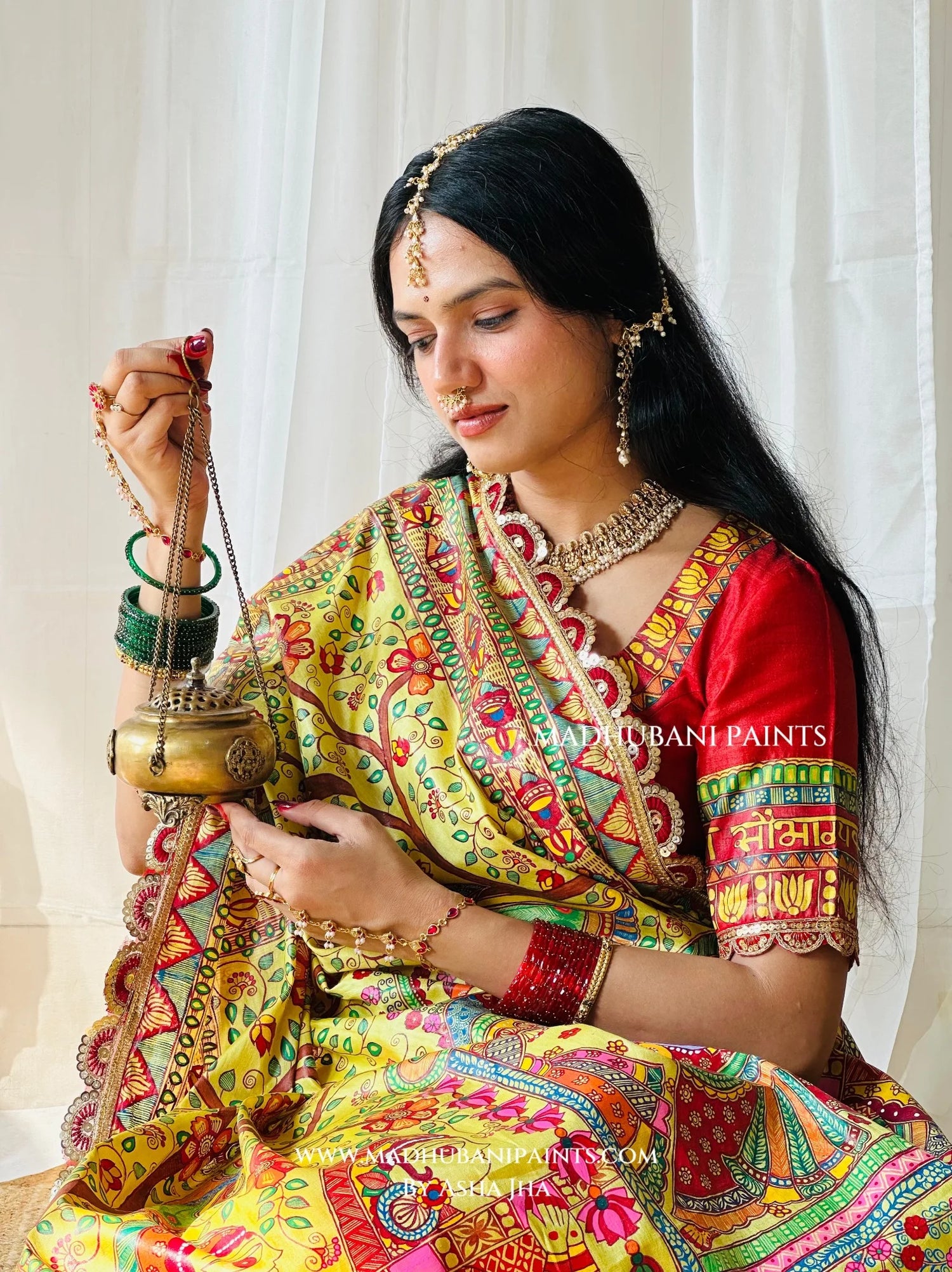 Yellow Devi Ki Sawari Madhubani saree with traditional doli procession painting and decorative lotus border beside festive puja flowers.