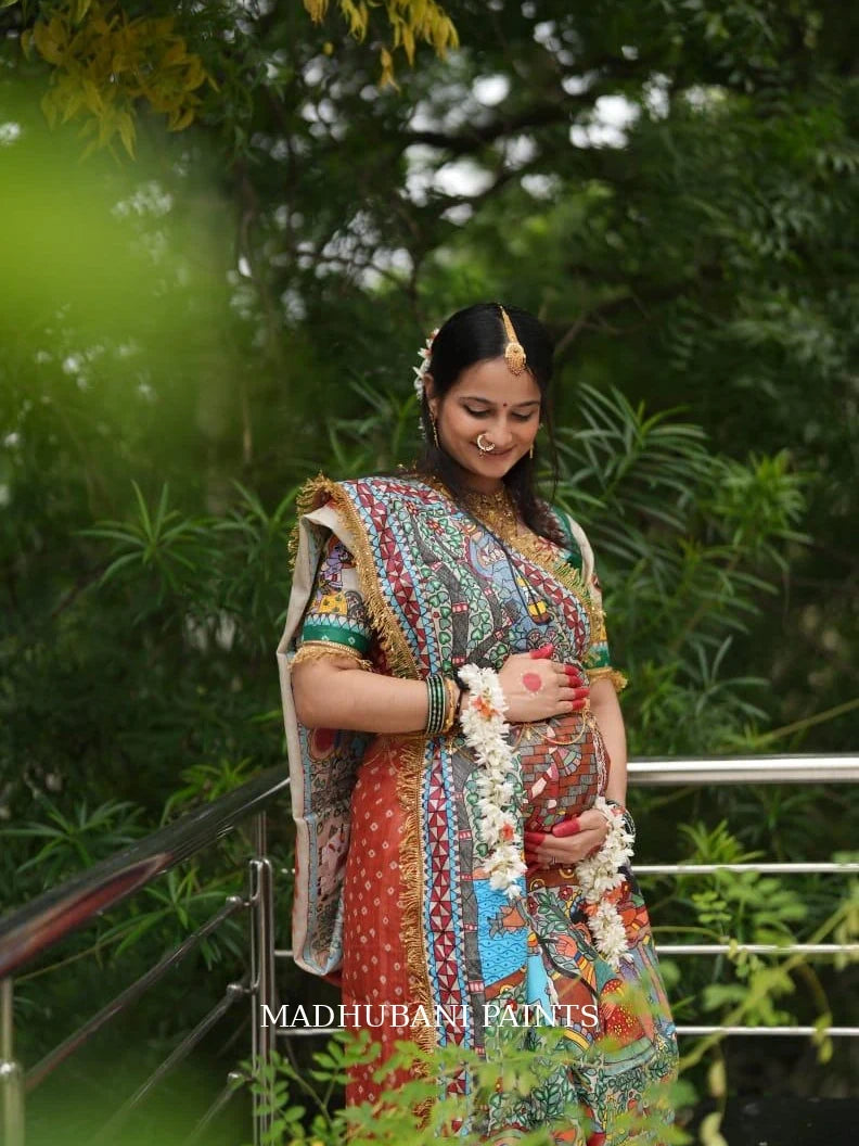 Expectant mother wearing a colorful hand-painted Madhubani Godh Bharai saree, celebrating motherhood with traditional floral jewelry