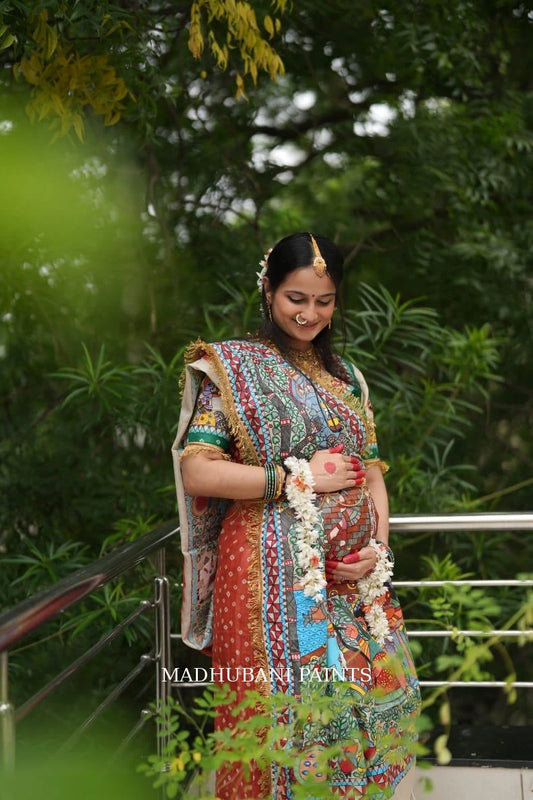 Expectant mother wearing a colorful hand-painted Madhubani Godh Bharai saree, celebrating motherhood with traditional floral jewelry