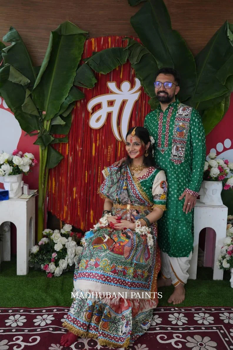 Couple celebrating pregnancy outdoors in a traditional Madhubani painting Godh Bharai saree and green kurta.