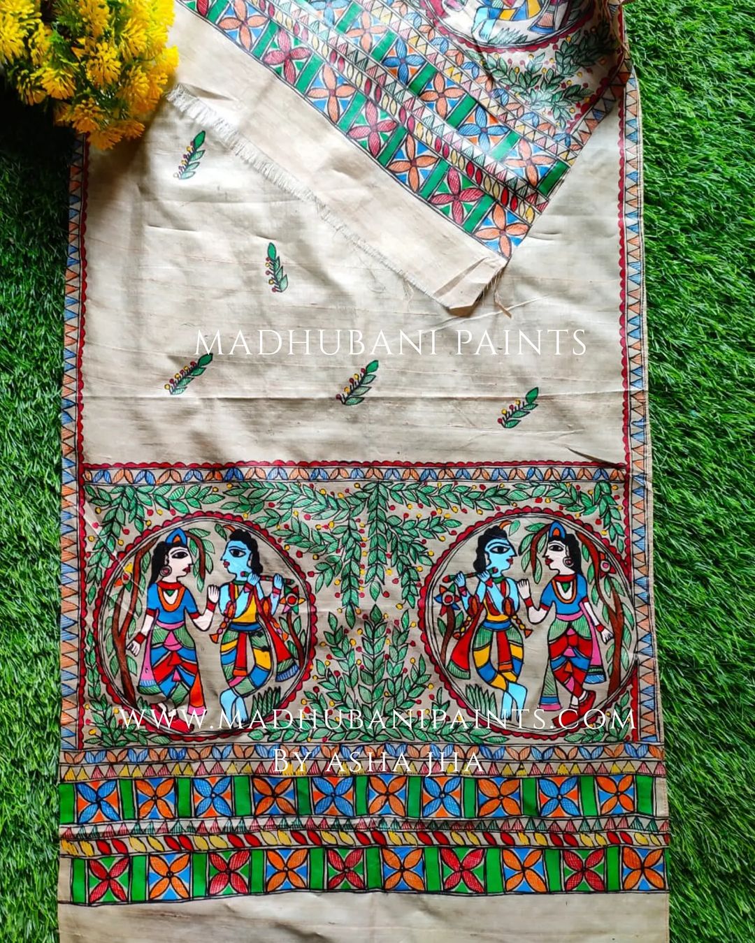 A beige handloom tussar silk stole with a traditional Madhubani artwork depicting Radha and Krishna in the center, surrounded by floral patterns.